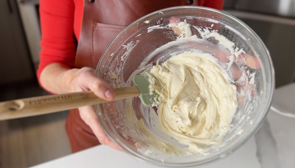 femme tenant un bol de glaçage au fromage à la crème avec maryse à la main, en train de mélanger